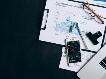 Top view of financial reports, smartphone showing stock market data, and a laptop on desk.