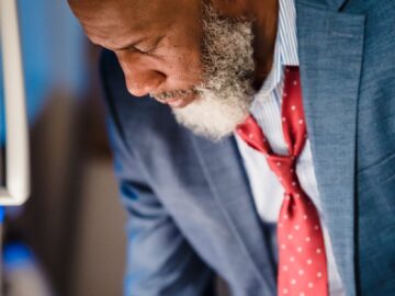 Close-up of a distinguished bearded man in a suit leaning over, focused and thoughtful.