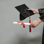 Close-up of graduate holding cap and diploma with red ribbon, symbolizing success.