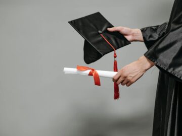 Close-up of graduate holding cap and diploma with red ribbon, symbolizing success.