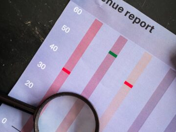 A magnifying glass on a vertical bar chart titled "Revenue report" showing monthly data analysis.