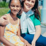 Mother and daughter smiling together in a sunny outdoor setting, embracing happiness and love.