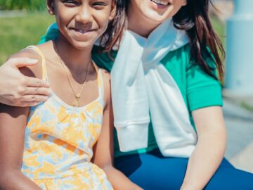 Mother and daughter smiling together in a sunny outdoor setting, embracing happiness and love.