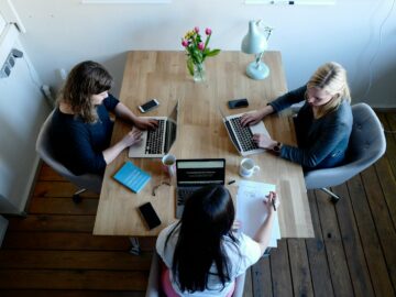 three women sitting around table using laptops
