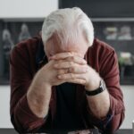 Elderly man with white hair contemplating past memories through a photo album at home.