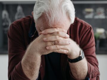 Elderly man with white hair contemplating past memories through a photo album at home.