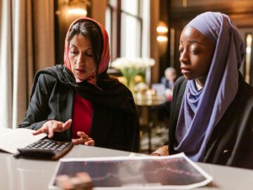 Two multicultural women collaborating on financial analysis using a calculator.