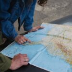A couple examines a map on a car's hood, planning their travel route.