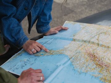 A couple examines a map on a car's hood, planning their travel route.