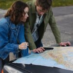 A young couple examines a map on a car hood, planning their next travel destination outdoors.