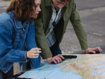 A young couple examines a map on a car hood, planning their next travel destination outdoors.