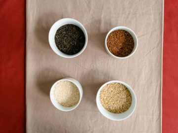 Four types of rice elegantly displayed in white bowls on a fabric surface.