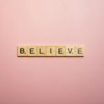 Wooden letter tiles spell 'Believe' on a soft pink background, inspiring positivity.