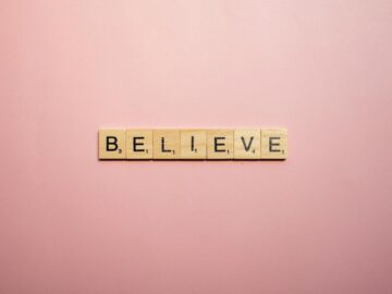 Wooden letter tiles spell 'Believe' on a soft pink background, inspiring positivity.