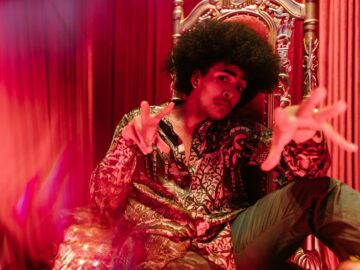 Man in vibrant outfit and afro hairstyle posing in a creative indoor setting.