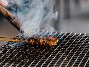 Close-up of juicy skewered meat grilling with smoke rising on a barbecue.