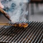 Close-up of juicy skewered meat grilling with smoke rising on a barbecue.