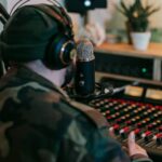 Musician recording sound in studio with headphones and mixer, focused on creative audio production.
