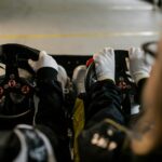 Close-up view of go-kart racers driving with gloves gripping steering wheels indoors.