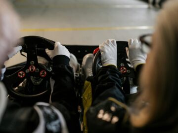 Close-up view of go-kart racers driving with gloves gripping steering wheels indoors.