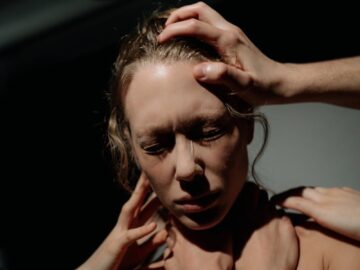 Dramatic lighting on a woman expressing deep emotional distress, surrounded by hands.