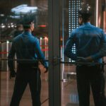 Security guards standing by glass doors, protecting a building entrance at night.