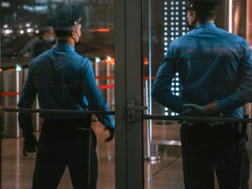 Security guards standing by glass doors, protecting a building entrance at night.