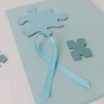 Close-up of blue puzzle pieces and a ribbon symbolizing Autism Awareness on a pastel background.