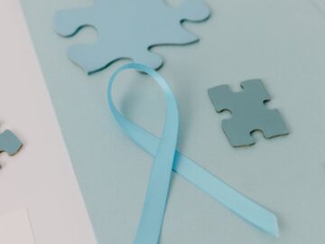 Close-up of blue puzzle pieces and a ribbon symbolizing Autism Awareness on a pastel background.