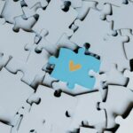 A standout blue puzzle piece with a heart symbol among white puzzle pieces, showing uniqueness.