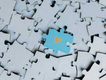A standout blue puzzle piece with a heart symbol among white puzzle pieces, showing uniqueness.