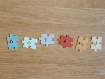Colorful puzzle pieces spelling 'autism' on a wooden surface, promoting autism awareness.