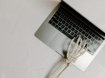 Skeleton hand on laptop keyboard overlaid on papers, symbolizing burnout.