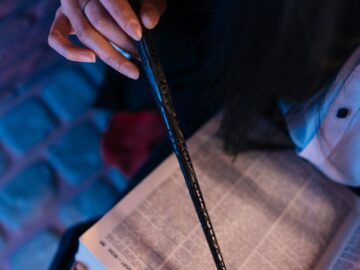 Close-up of a person holding a wand while reading an open book with focused lighting.