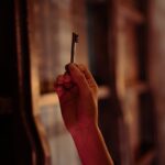 A hand holding an antique key is seen in a dimly lit room, evoking mystery and intrigue.