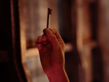 A hand holding an antique key is seen in a dimly lit room, evoking mystery and intrigue.