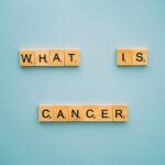 Wooden letter tiles form the question 'What is cancer?' on a blue background.