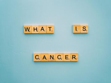 Wooden letter tiles form the question 'What is cancer?' on a blue background.