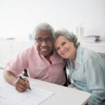 Happy elderly couple sitting at a desk, smiling and signing documents. Perfect for insurance and lifestyle themes.