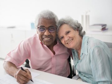 Happy elderly couple sitting at a desk, smiling and signing documents. Perfect for insurance and lifestyle themes.