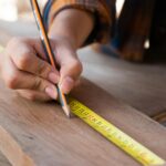 Close-up of hands using a measuring tape and pencil, highlighting precision in carpentry work.