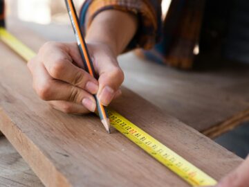 Close-up of hands using a measuring tape and pencil, highlighting precision in carpentry work.
