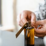 Hands label an amber glass bottle of essential oil. Aromatherapy and skincare concept.