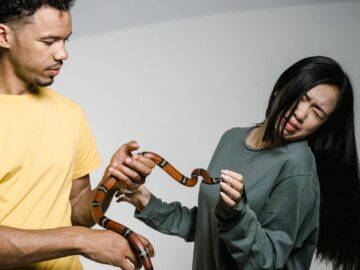 A man and woman holding a snake showing mixed expressions, illustrating phobia and curiosity.