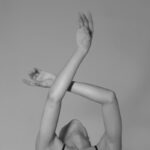 A graceful dancer in a monochrome image with arms elegantly crossed above the head.
