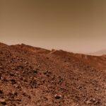 A barren and rocky desert landscape reminiscent of the planet Mars with a warm, dusty sky.