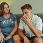 A mother and son engage in a deep conversation on the living room couch, conveying strong emotions.