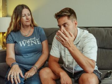 A mother and son engage in a deep conversation on the living room couch, conveying strong emotions.