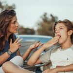 A mother and her teenage son are having a conversation outdoors. The son appears disinterested.