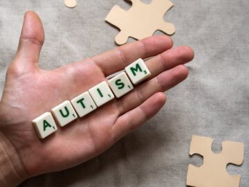 Conceptual image showing a hand holding 'autism' tiles among puzzle pieces, signifying autism awareness.
